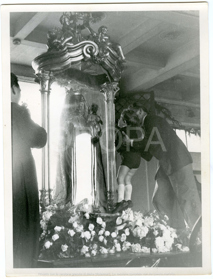 [94528] Un bambino visto di spalle viene sollevato per baciare la teca contenente la statua.