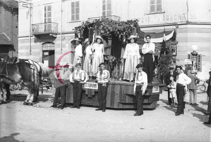 Biella, anni ‘30. Festa dell’Uva. Il carro allegorico dei Littoriani in sosta in piazza Cossato al Vernato. Sull’edificio campeggia sbiadita l’insegna della storica trattoria Aurora (Archivio Cesare Valerio - Proprietà Fondazione Cassa di Risparmio di Biella)
