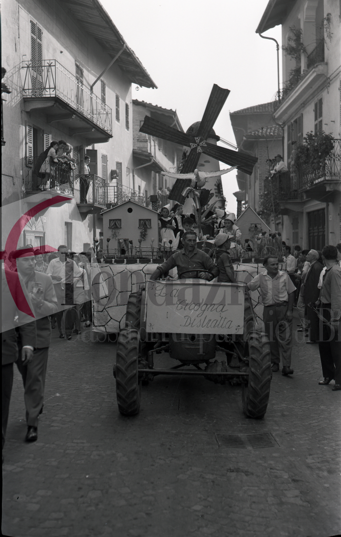 Masserano, 24 settembre 1961. Festa dell’Uva. Un carro allegorico in via Roma. Nel cesto della “Cicogna Distratta” invece di un neonato c’è una bottiglia di vino! (Archivio Lino Cremon - Proprietà Fondazione Cassa di Risparmio di Biella)